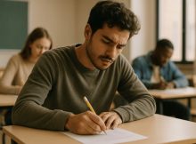 Pessoa concentrada fazendo uma prova em uma sala de aula iluminada naturalmente, com outros alunos ao fundo, transmitindo foco e ambiente educacional realista